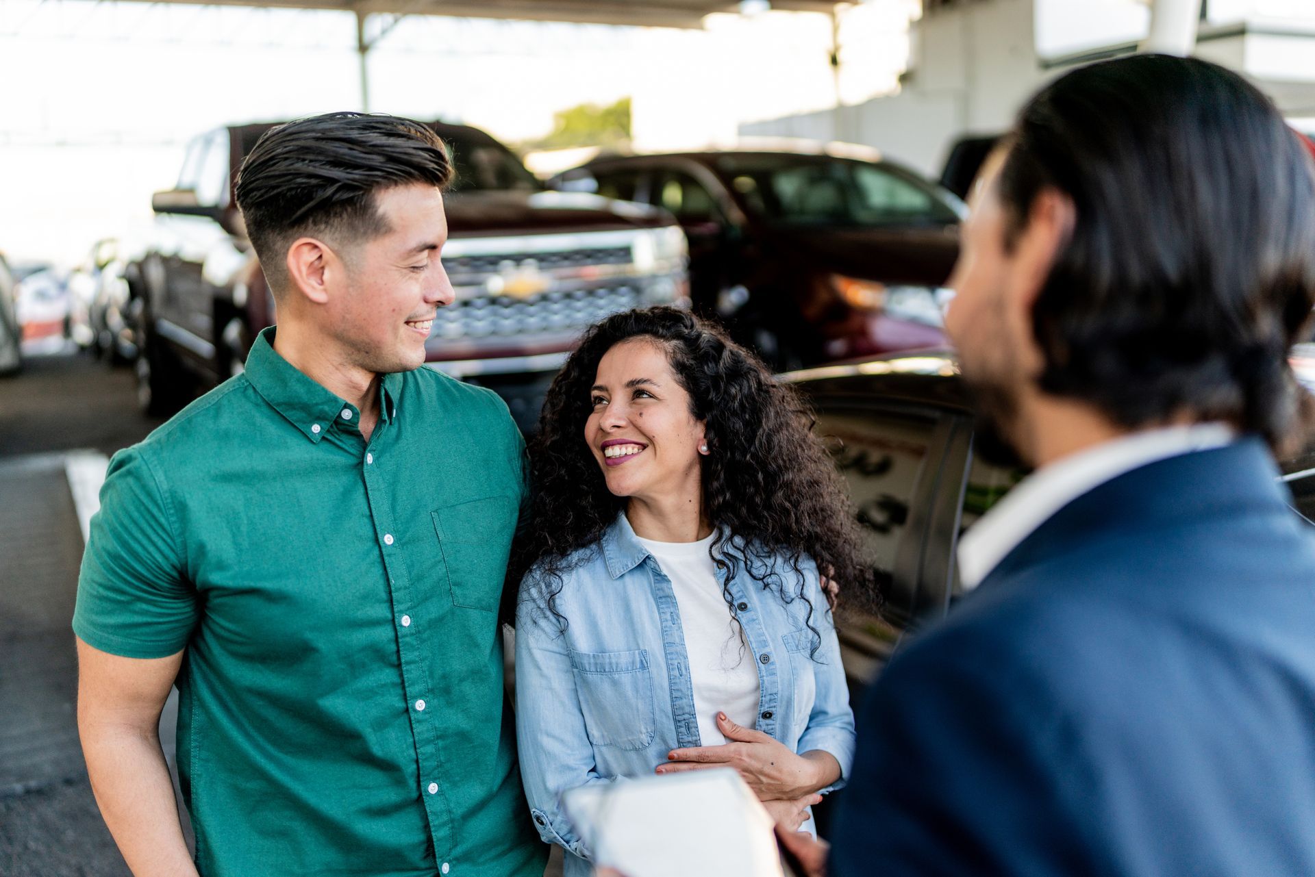A man and woman are standing next to each other in front of a car dealership.