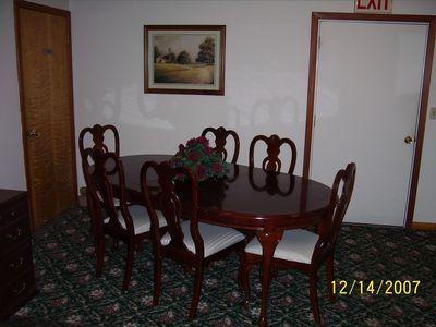 A dining room with an oval wooden table and six matching chairs, situated on patterned carpet beneath a framed painting.