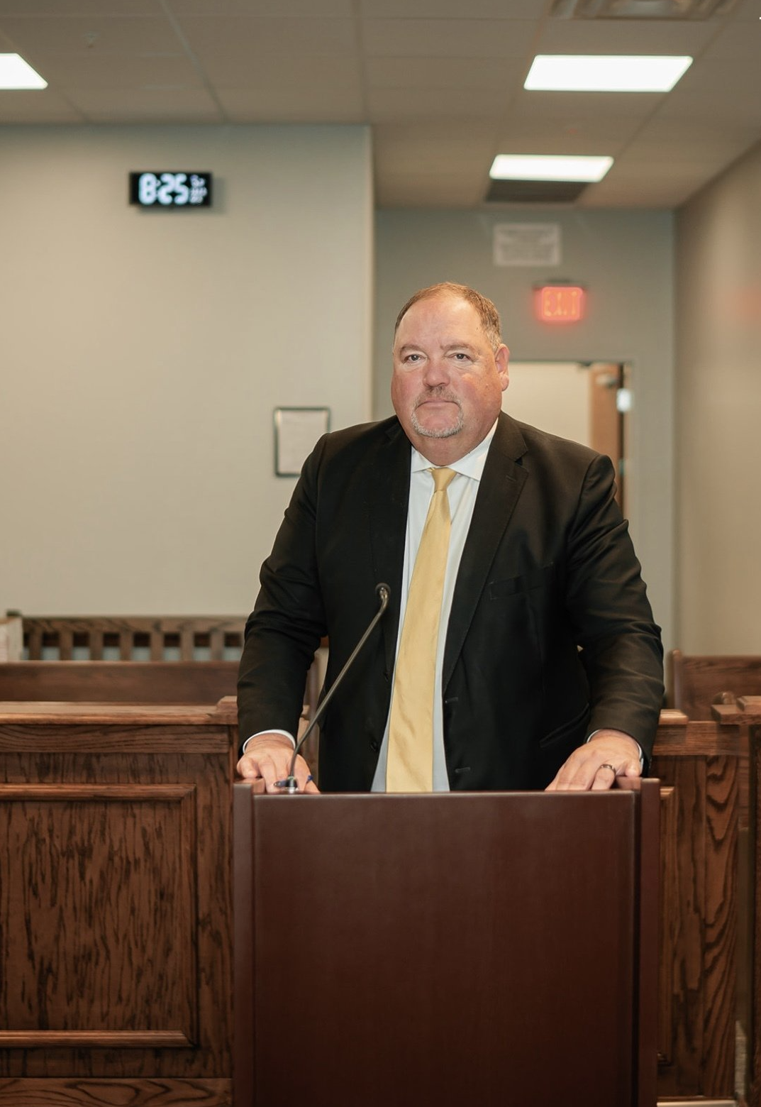 A man in a suit and tie is standing at a podium in a courtroom.