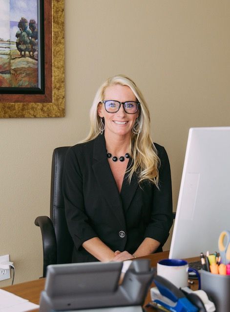 A woman wearing glasses is sitting at a desk in front of a computer.