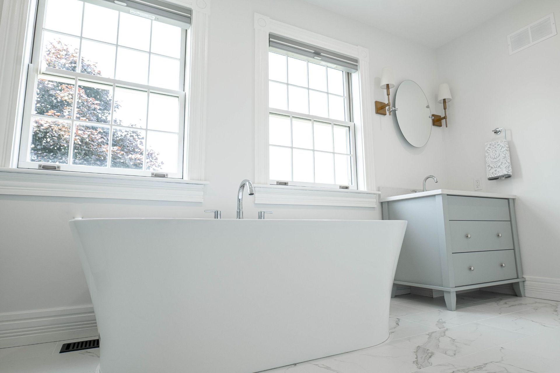 Bright white bathroom with a freestanding tub, windows, and a light blue vanity.