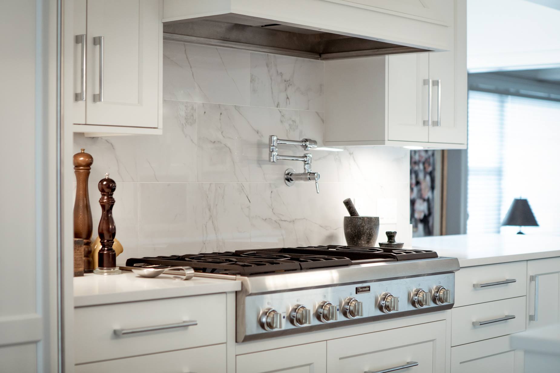 White kitchen with stove, range hood, marble backsplash, and cabinets.