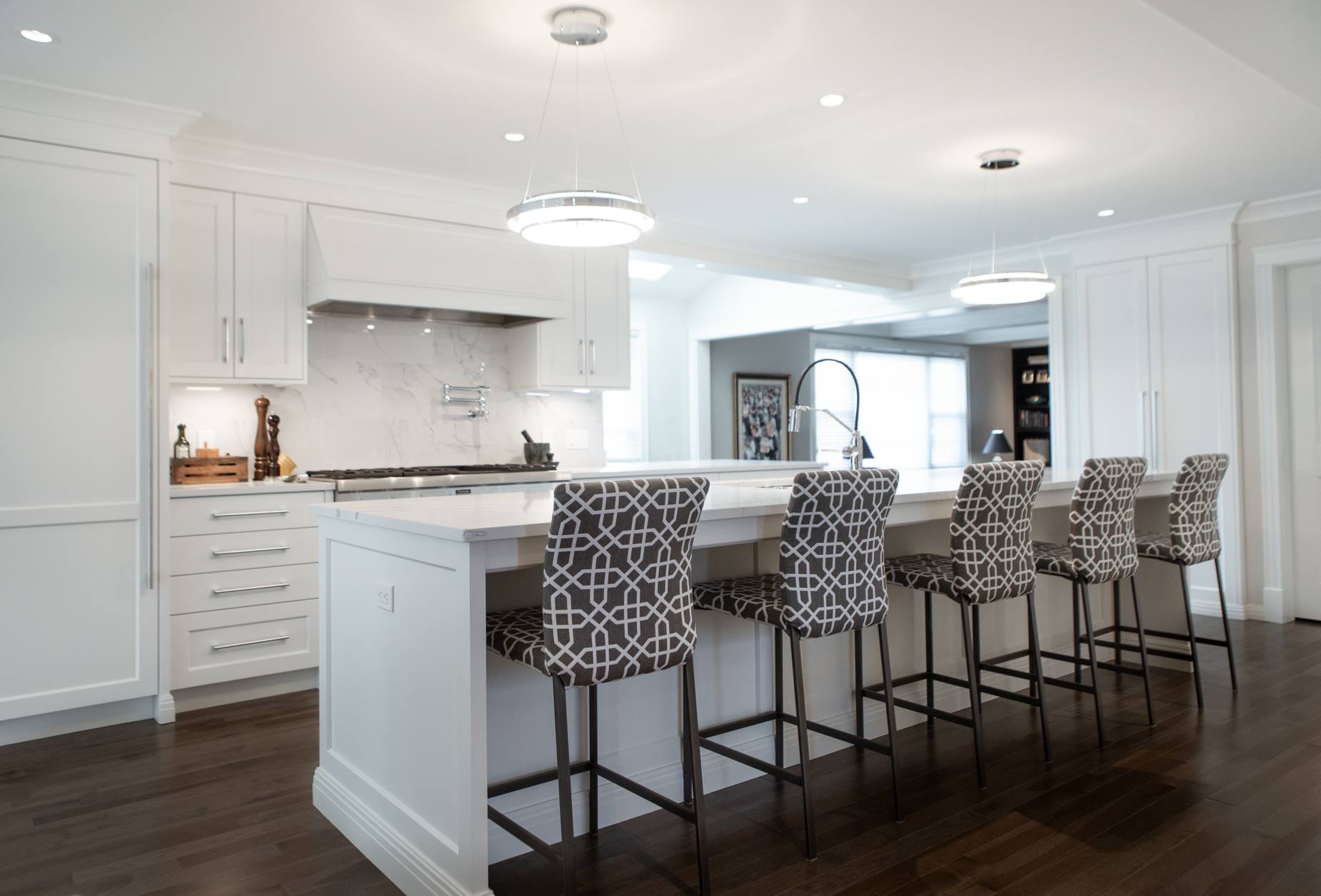 White kitchen with a central island, patterned bar stools, and dark wood floors.