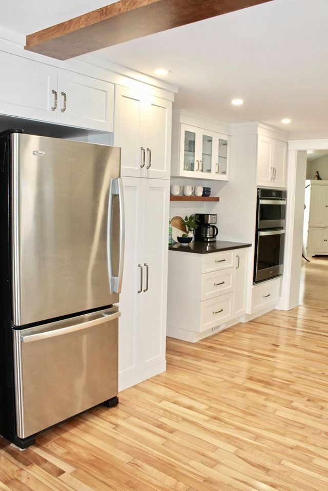 Stainless steel refrigerator and white kitchen cabinets. Wooden floor and beam ceiling.
