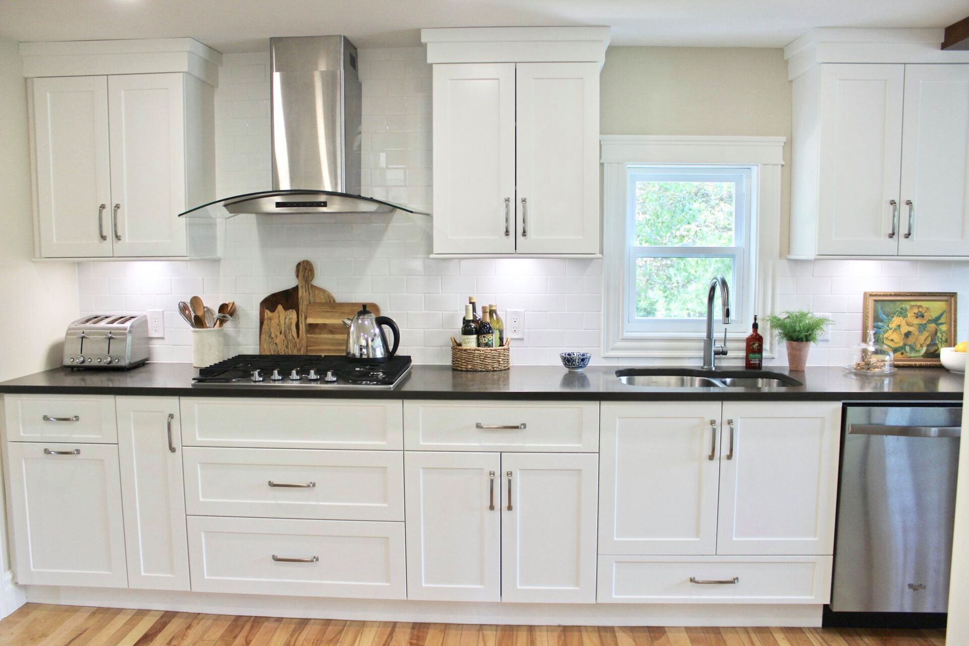White kitchen with black countertops, stainless steel appliances, and a window.