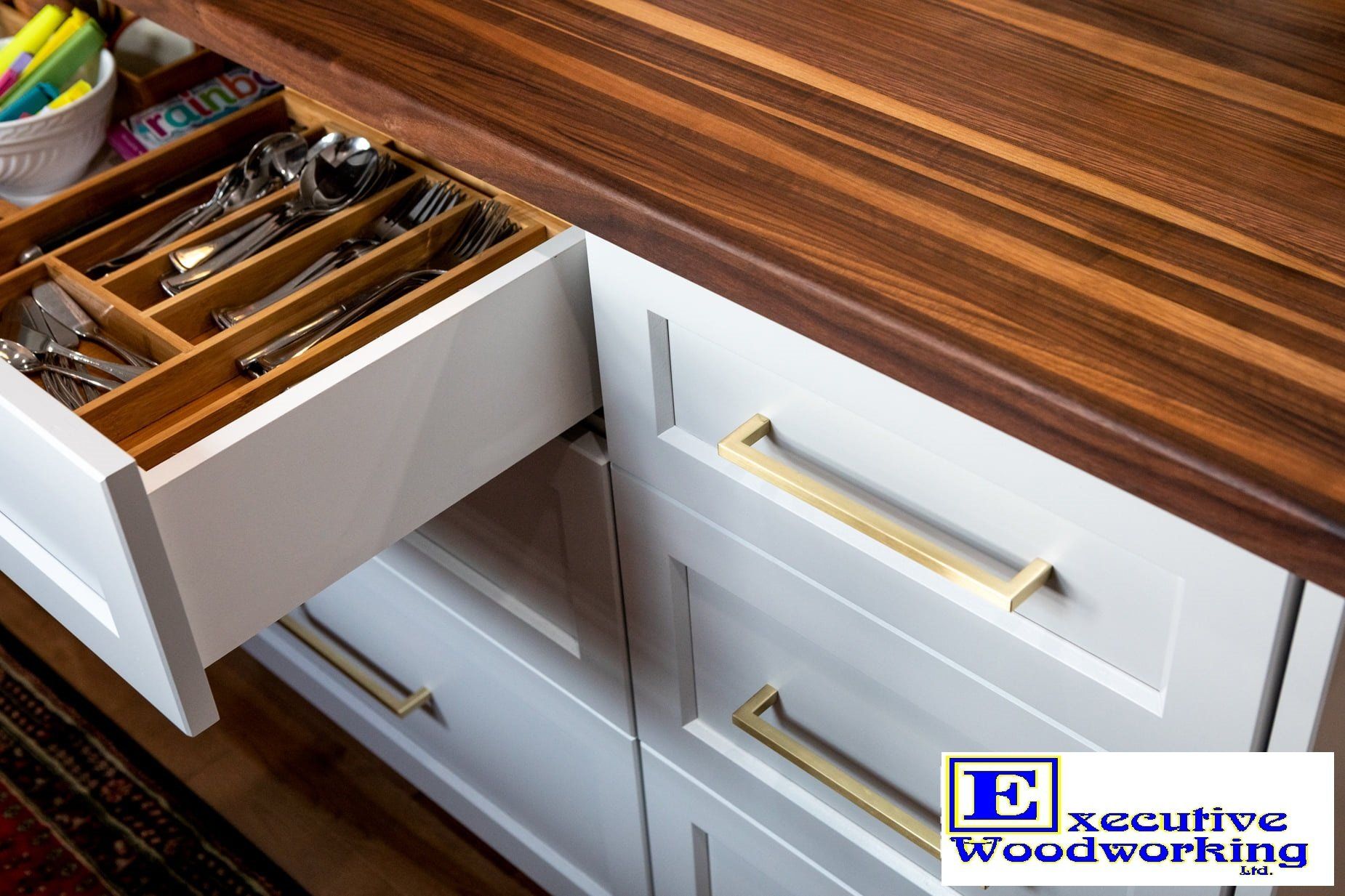 White kitchen drawers with a walnut countertop, one drawer open showing silverware.