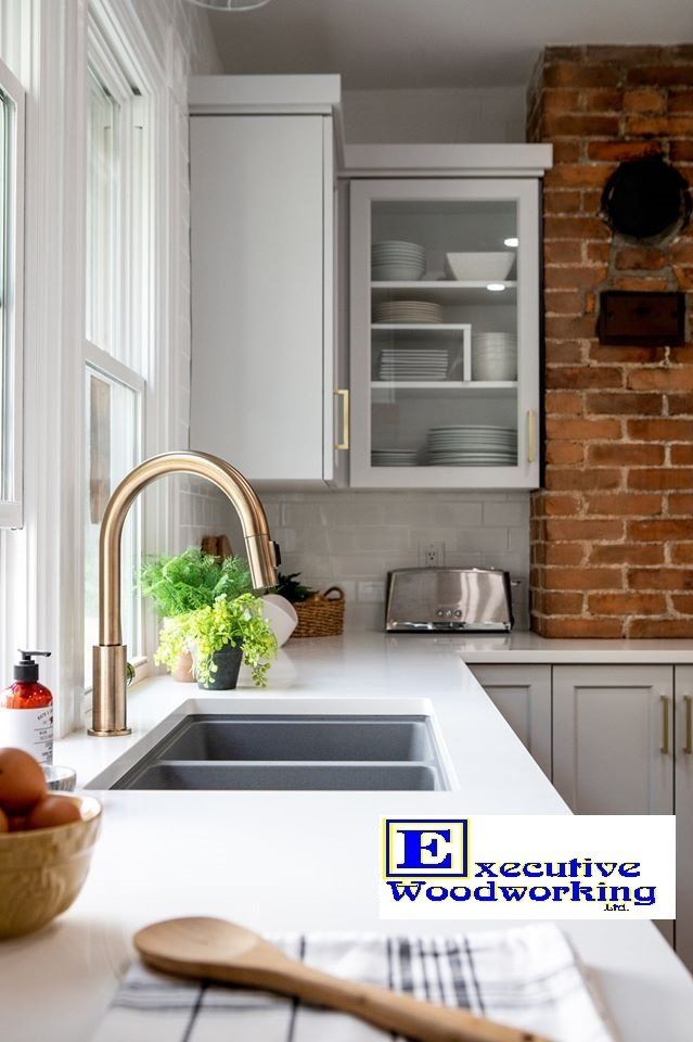 Modern kitchen with white cabinets, gold faucet, and brick wall.