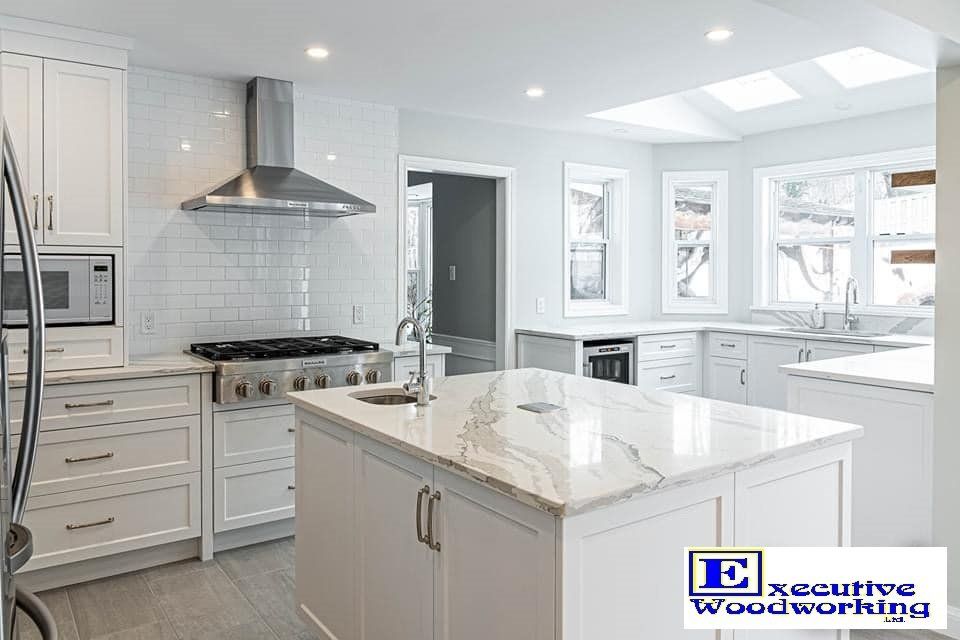 Modern white kitchen with island, stainless steel appliances, and natural light from skylight.