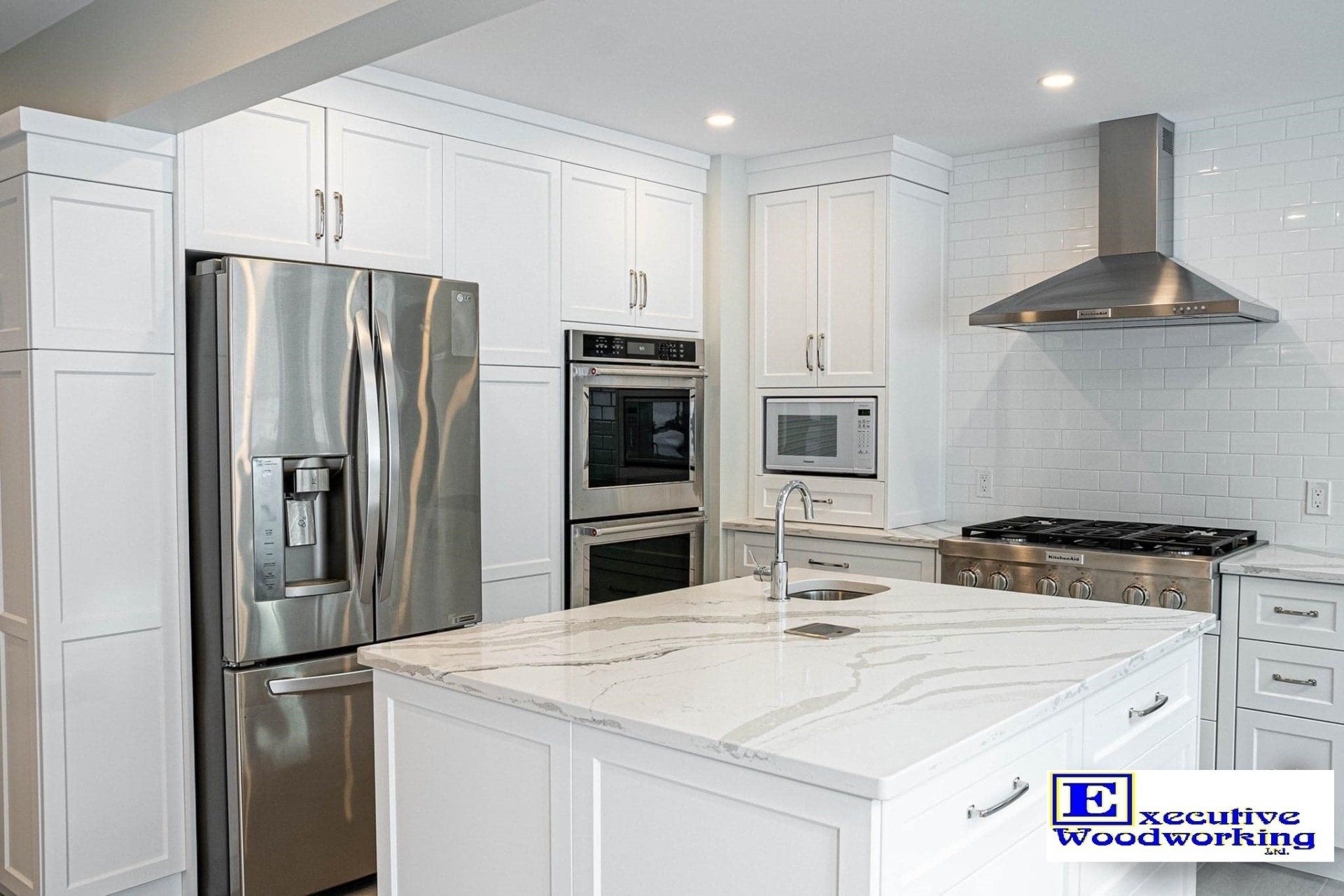 Modern white kitchen with stainless steel appliances, white cabinets, and a marble island.