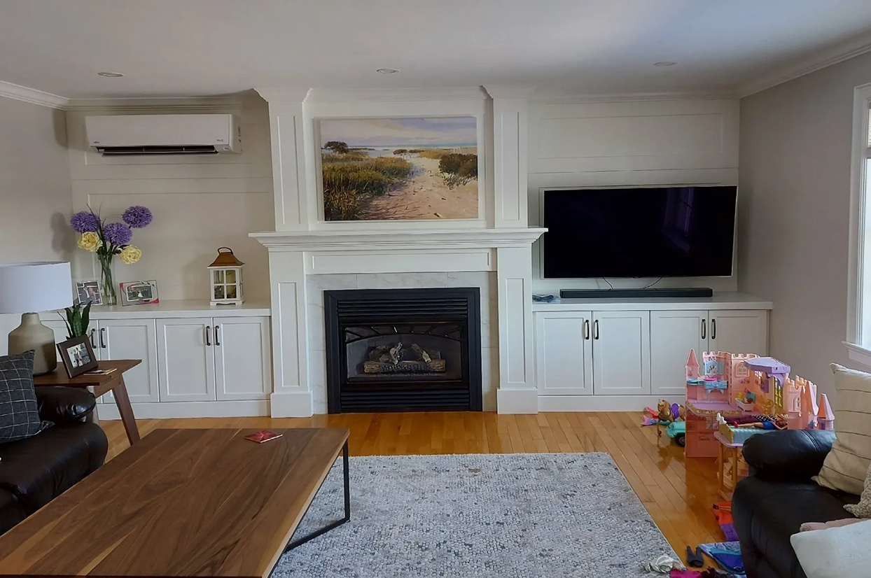 Living room with fireplace, built-ins, TV, artwork, hardwood floor, and children's toys.