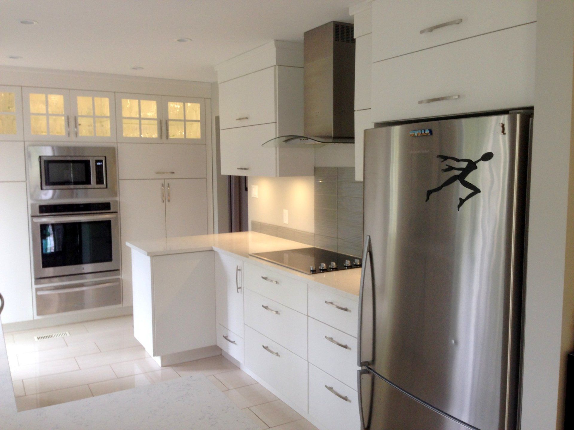 Modern white kitchen with stainless steel appliances and a running figure sticker on the refrigerator.