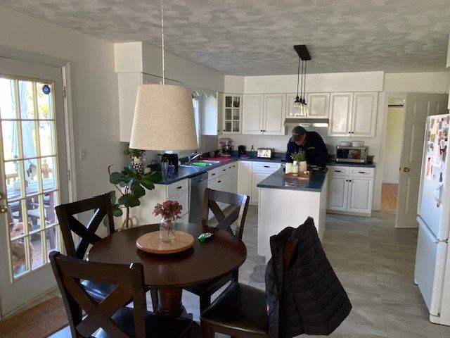 Kitchen with white cabinets, dark countertops, a round table, and a person standing near the counter.