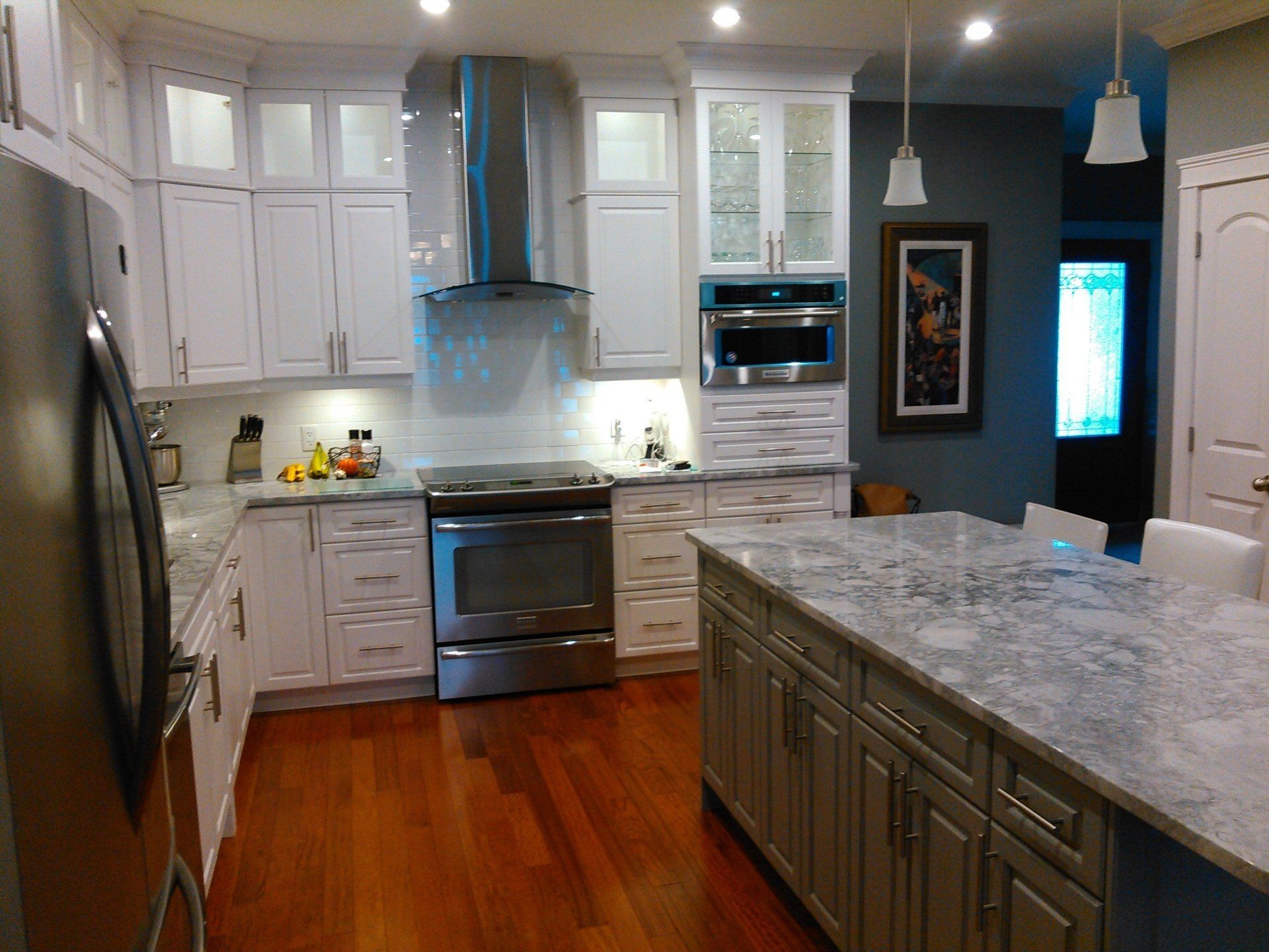 White kitchen with island, stainless steel appliances, and dark wood floors.