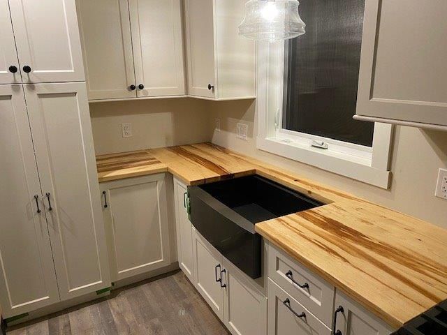 White kitchen with light wood countertops, black sink, and window.