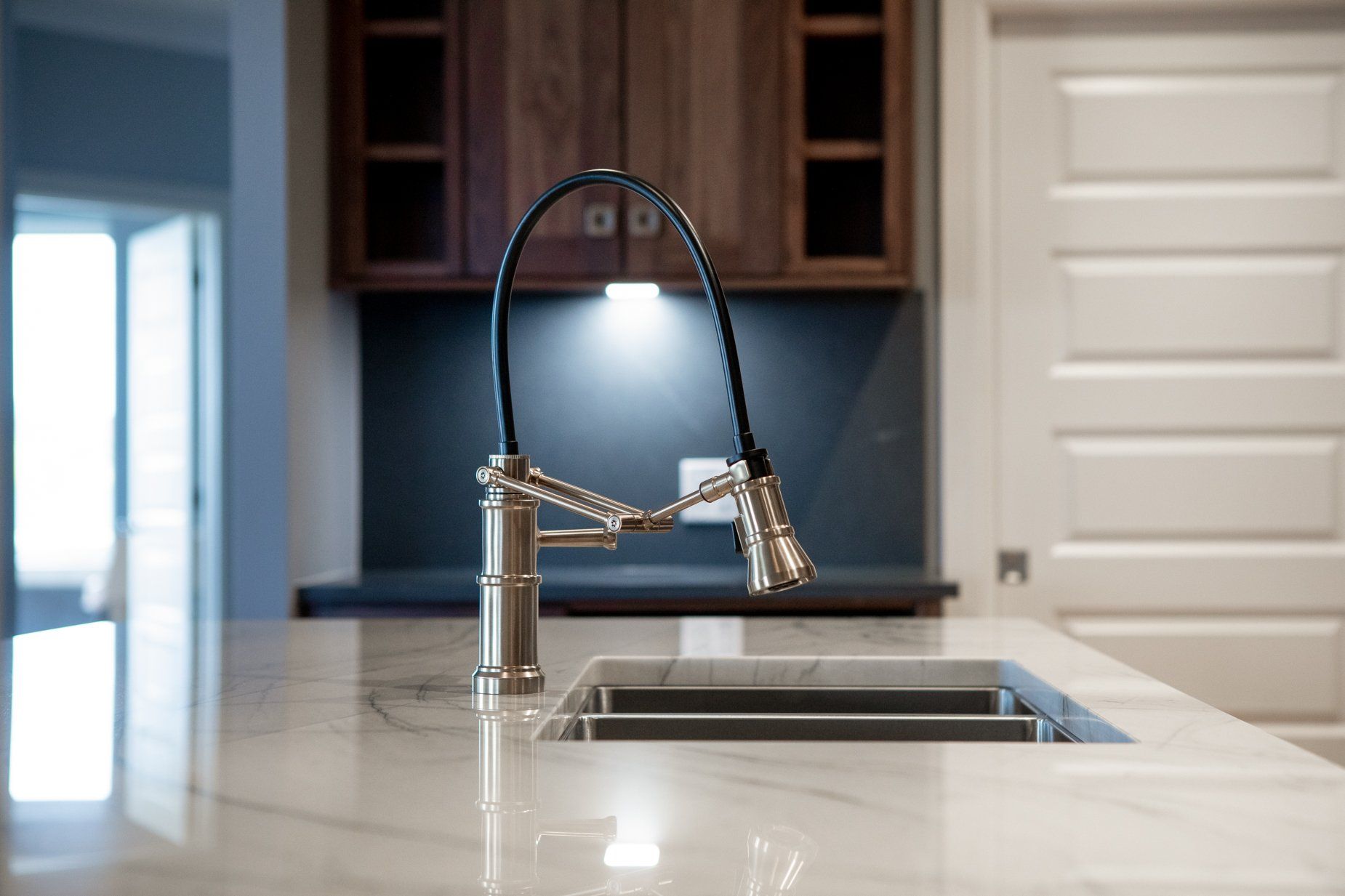 Kitchen sink with faucet, marble countertop, wooden cabinets, white door.