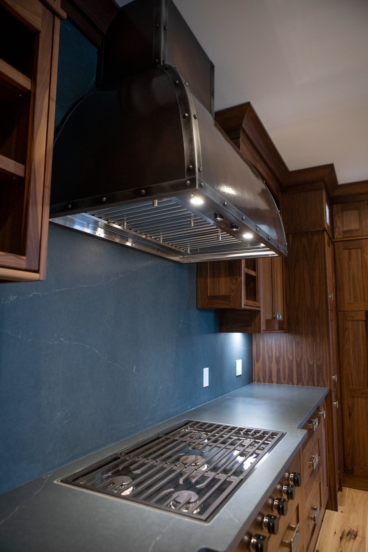 Kitchen with a stainless steel range hood, gas stove, and dark blue backsplash.