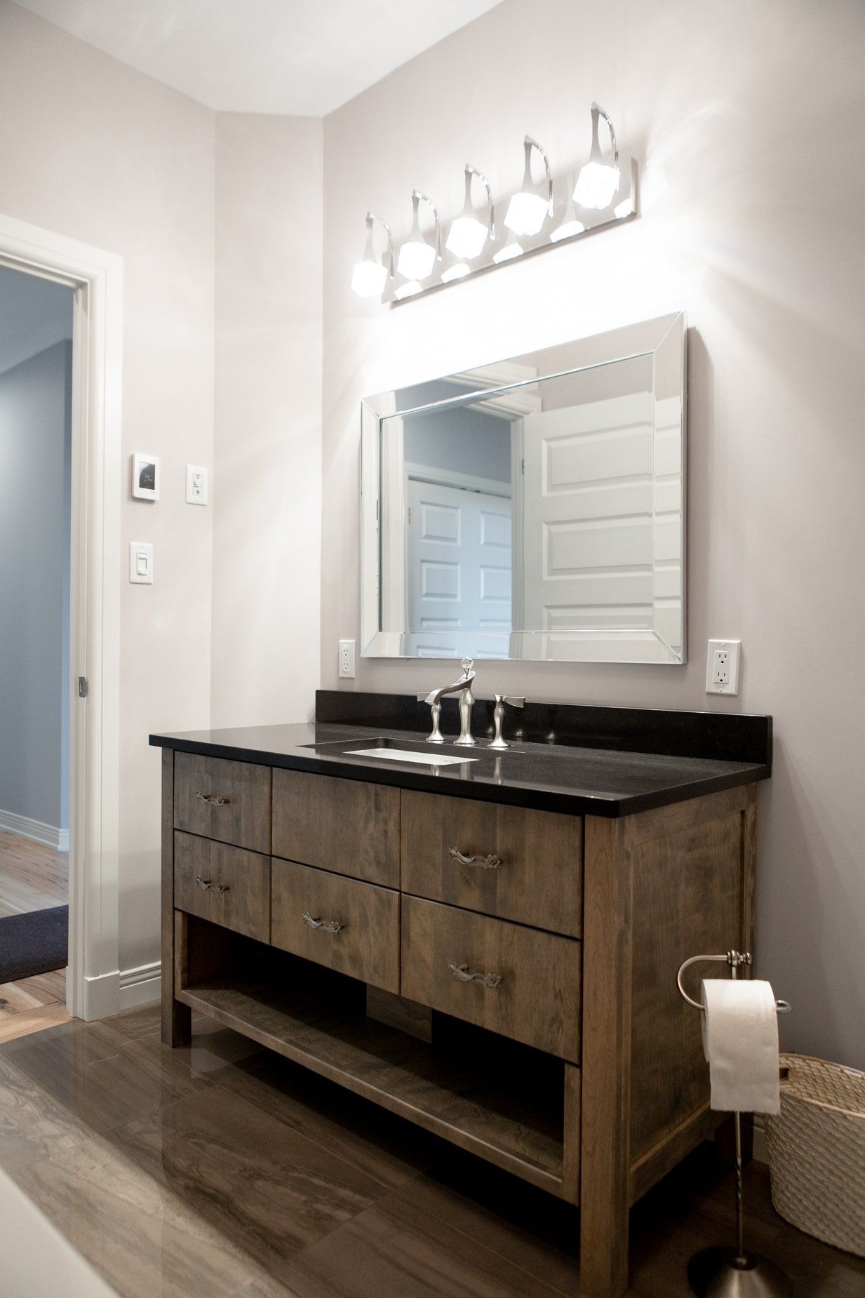 Bathroom with wooden vanity, black countertop, mirror, and light fixture.
