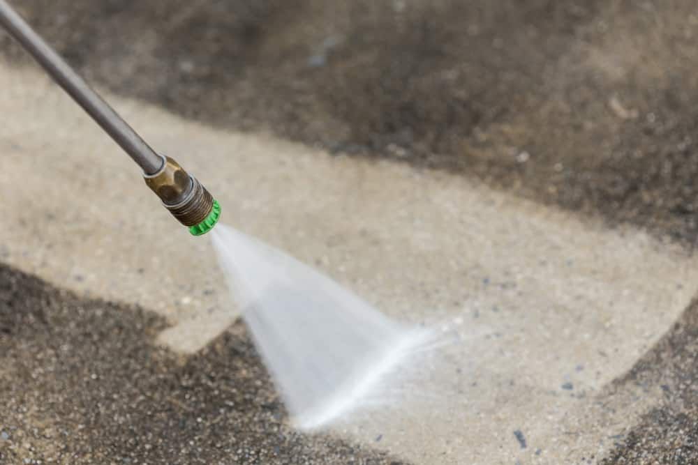 A Pressure Washer Nozzle Sprays a Fan of Water Onto a Dirty Concrete Surface — South Coast Pressure Washer in Gerringong, NSW