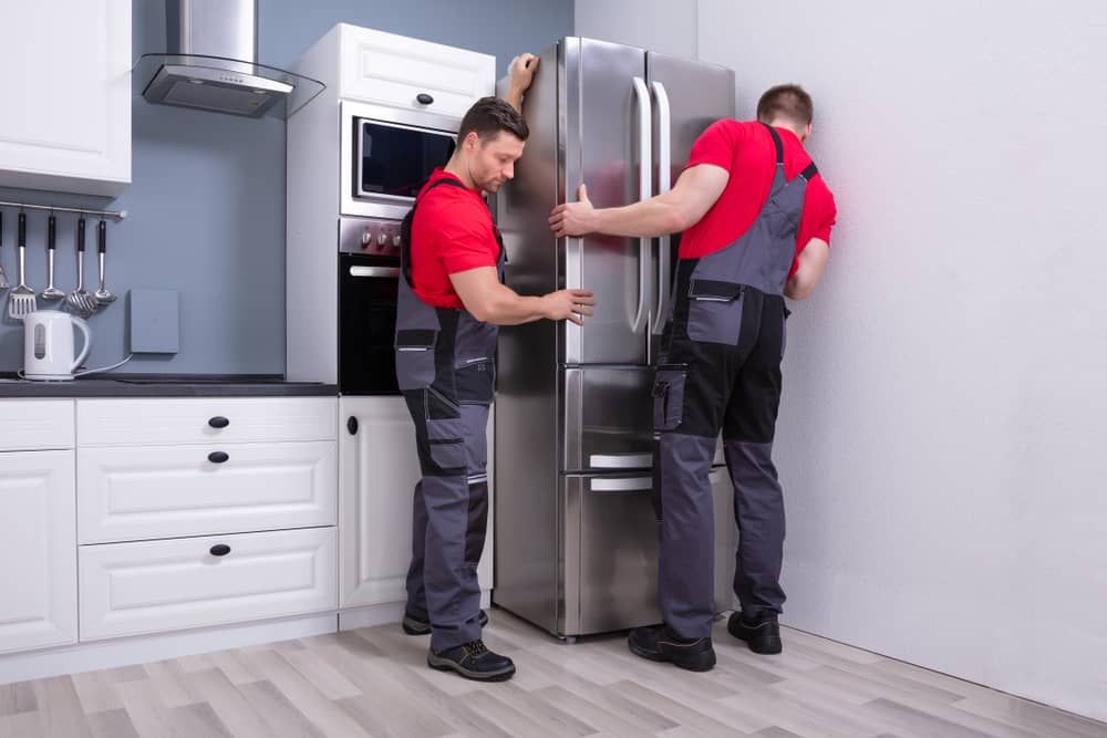 Two men are installing a refrigerator in a kitchen.