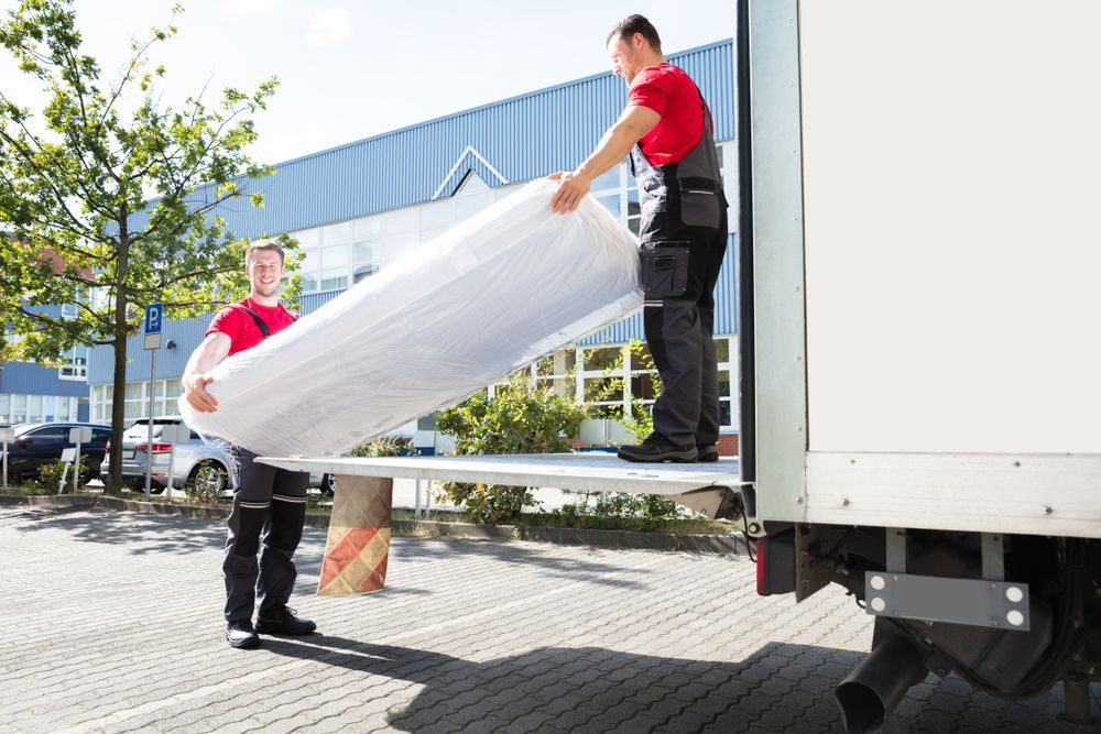 Two men are loading a mattress into the back of a truck.