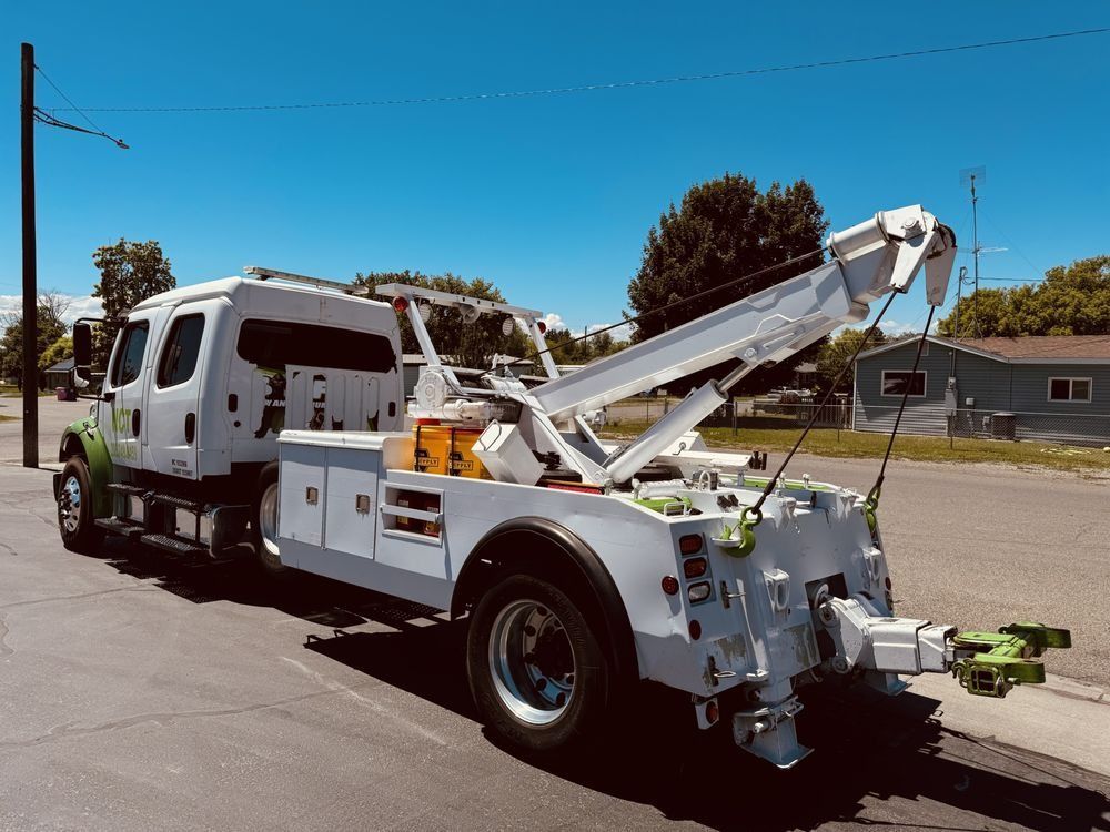 White tow truck with boom arm parked on a sunny street under a clear blue sky.