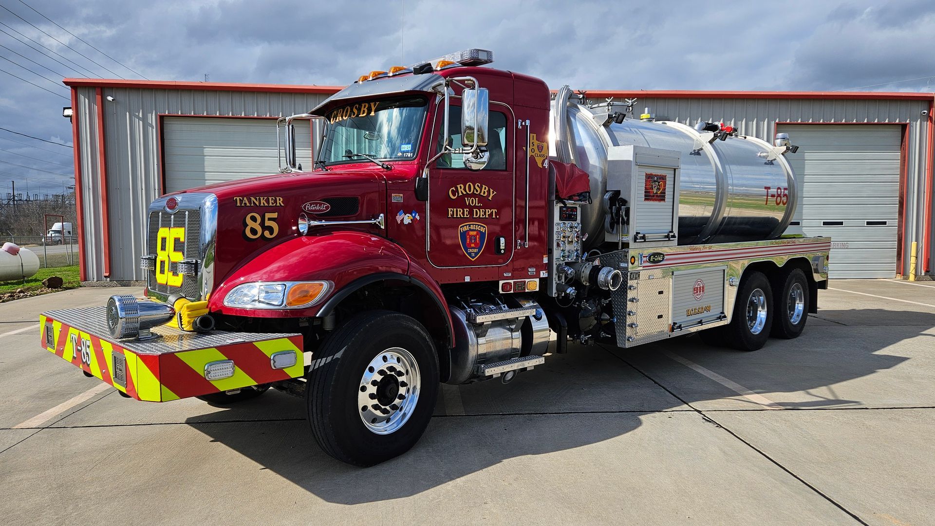 A fire tanker with the number 85 on the side is parked in front of a fire station.