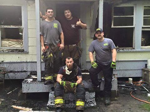 A group of firefighters are posing for a picture in front of a house.