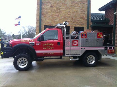 A red truck that says 'Crosby fire dept ' on the side is parked in front of a brick building
