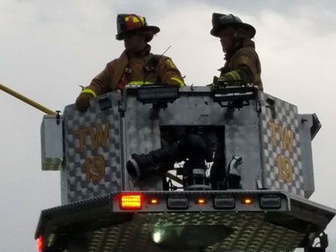 Two firefighters are sitting on top of a ladder truck