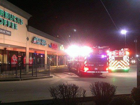 A fire truck is parked in front of a starbucks coffee shop at night.