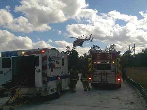 A life flight helicopter is flying over an ambulance and a fire truck.