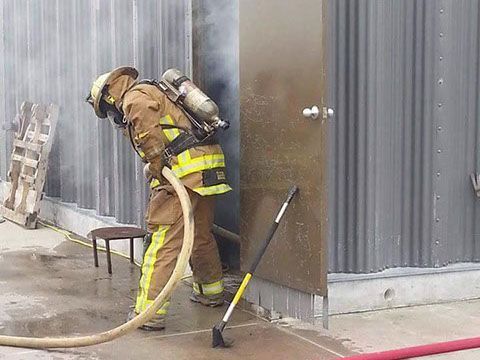 A fireman is standing next to a door with a hose during a training exercise.