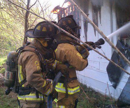 Two firefighters are spraying water on a house fire.