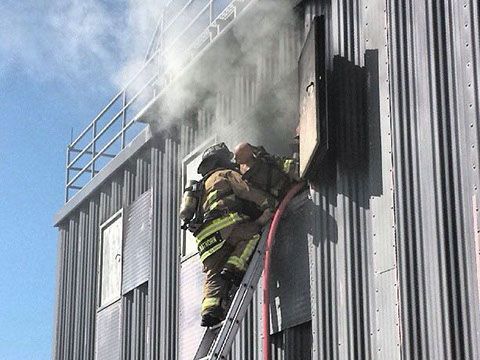 A fireman is climbing a ladder next to a window with smoke coming out of it during a training exercise.