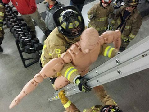 A fireman is training on rescue techniques by bringing a mannequin down a ladder.