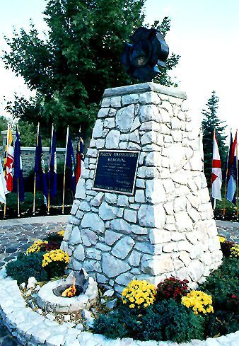 A stone statue with a plaque on it is surrounded by flowers and flags