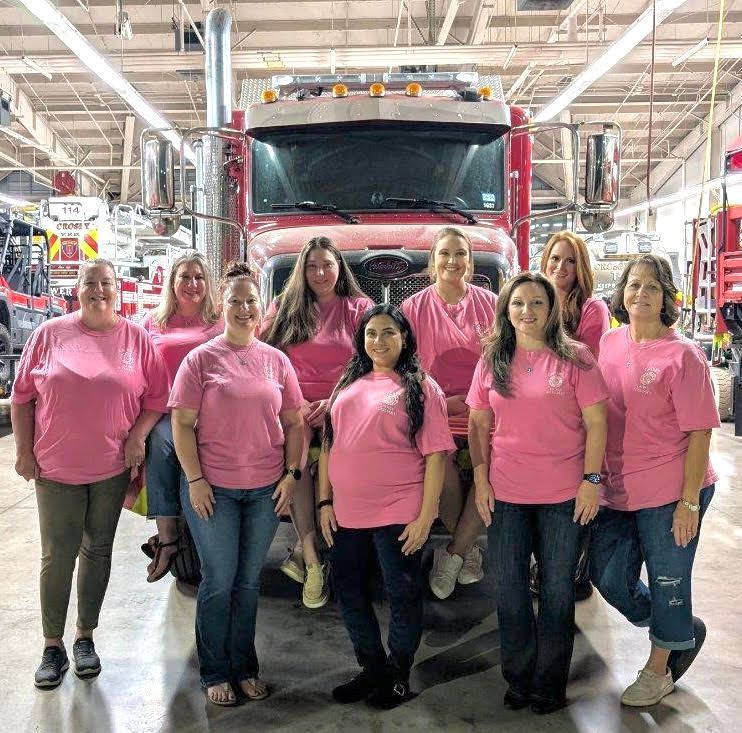 A group of women in pink shirts are posing for a picture in front of a fire truck.