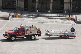A red fire truck is pulling a boat on a trailer in a parking lot.