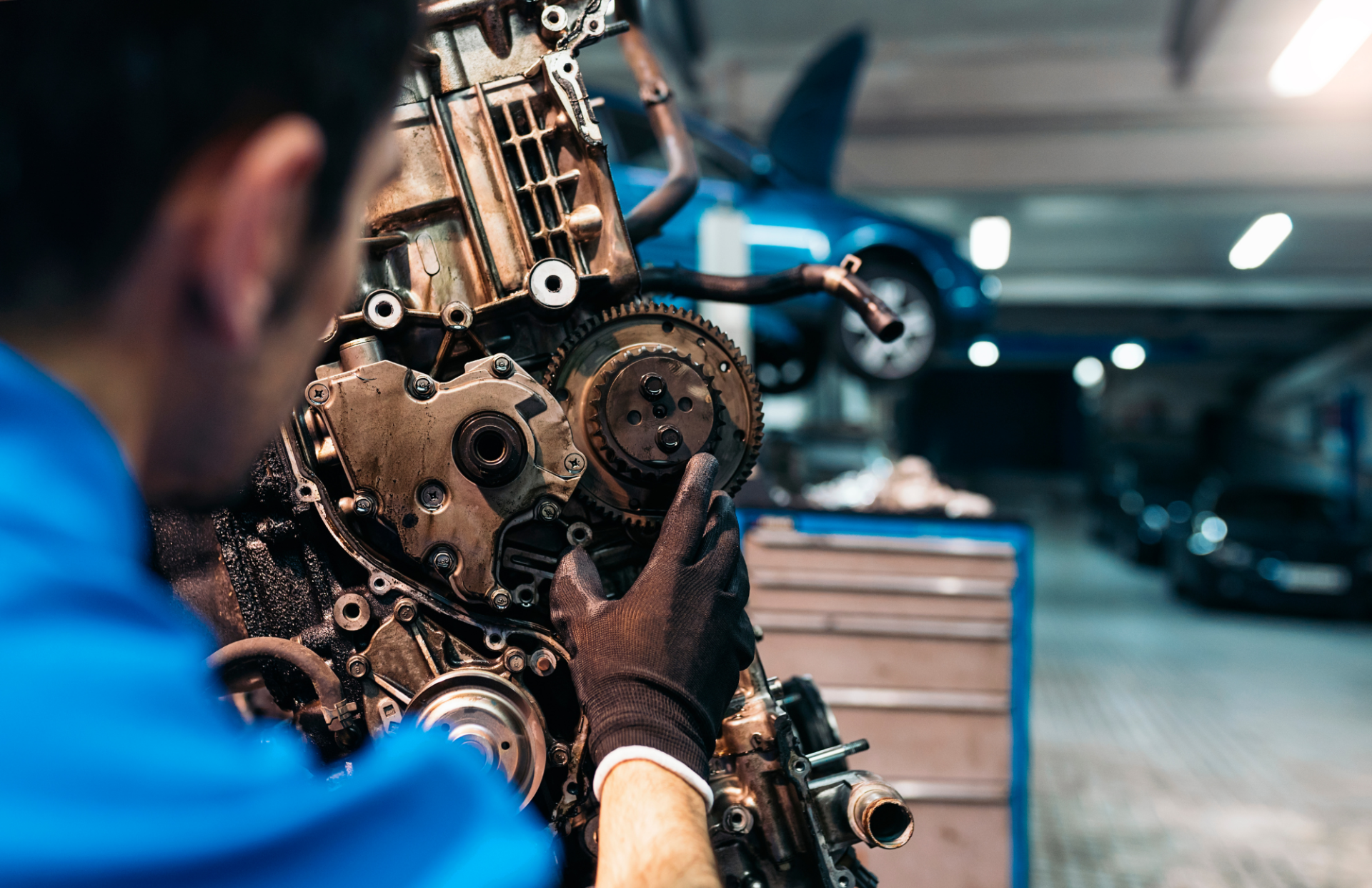Mechanic in blue shirt working on car engine in a garage.