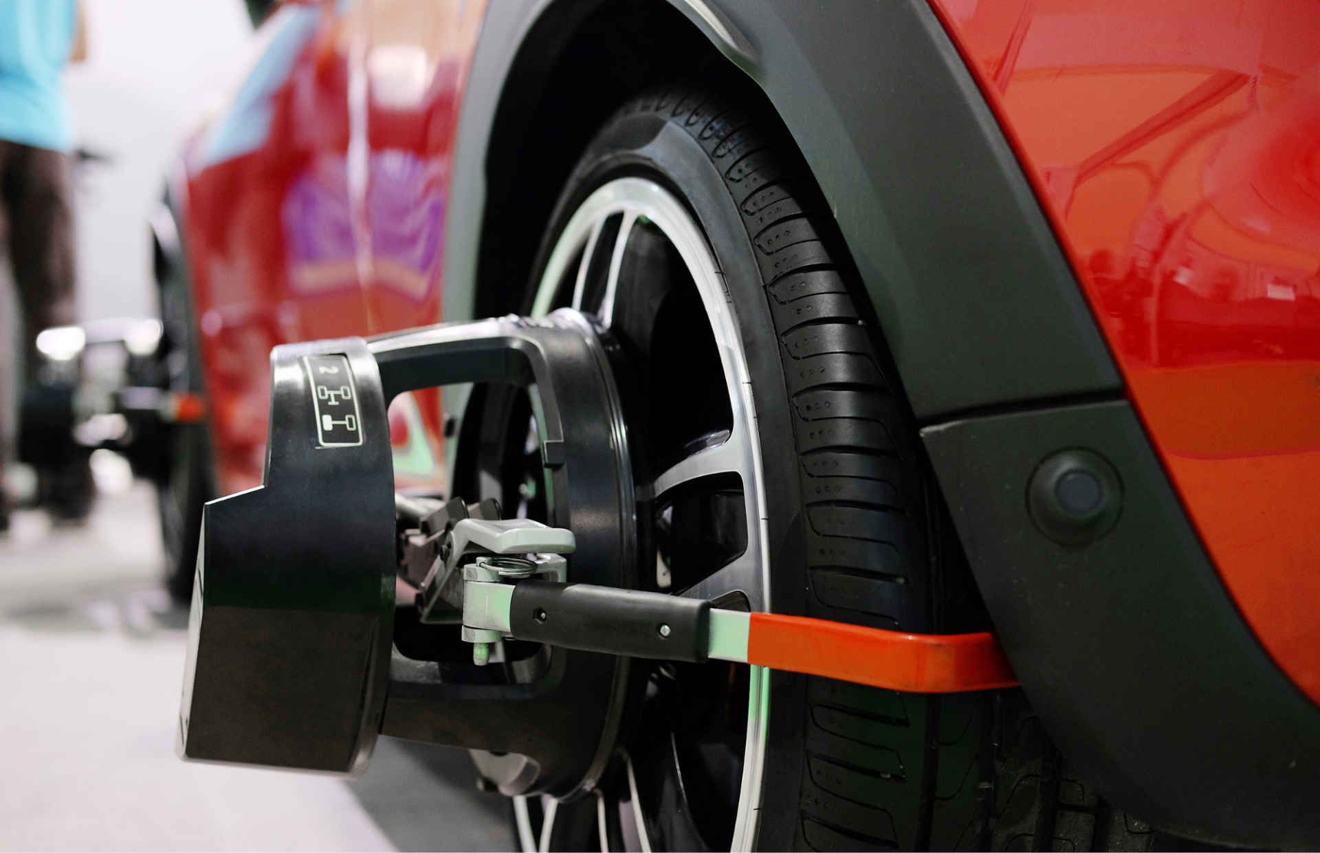 Wheel alignment equipment attached to the tire of a red car, likely in a shop.