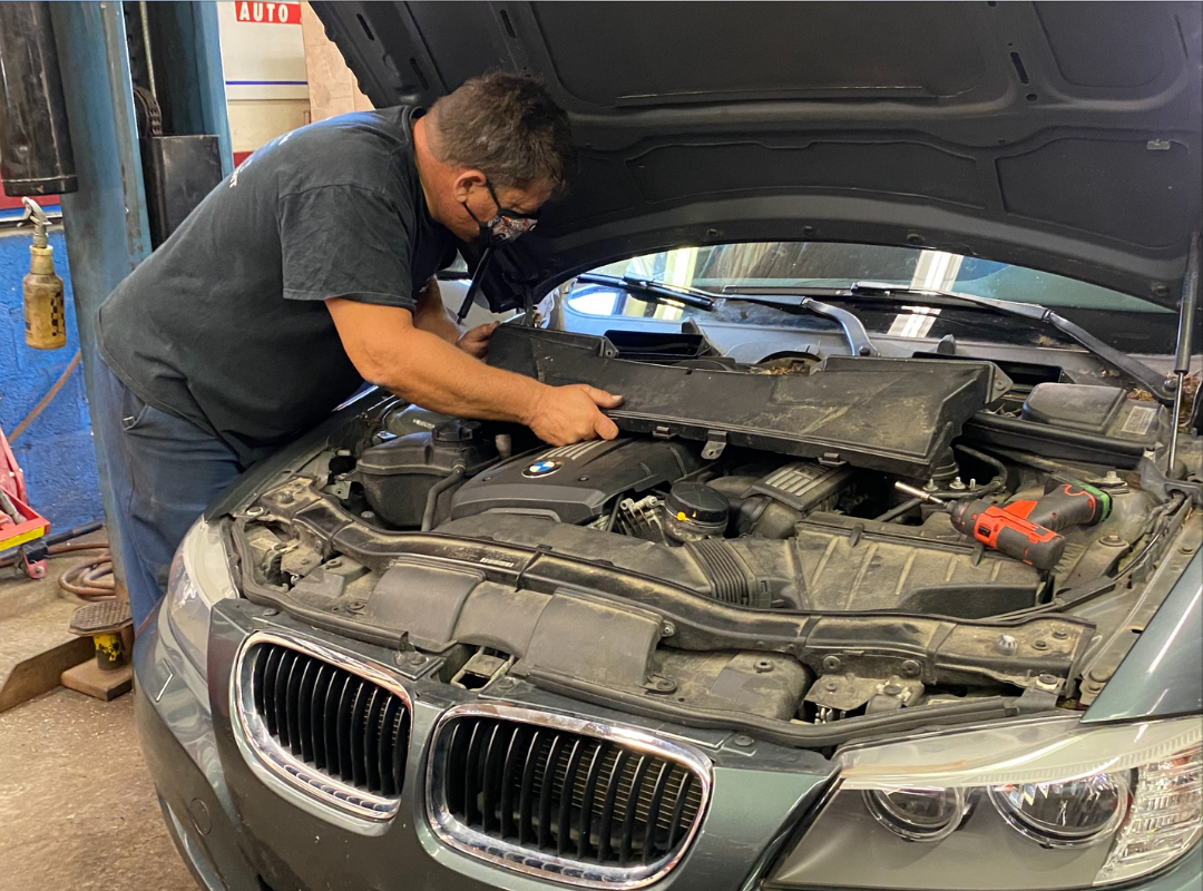 Mechanic working on the engine of a gray BMW car, under the open hood, indoors.