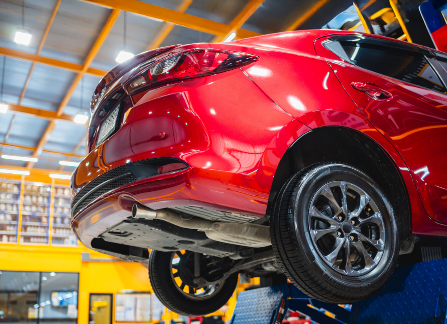 Red car on a lift in a garage, view from the rear, showing the undercarriage and exhaust system.