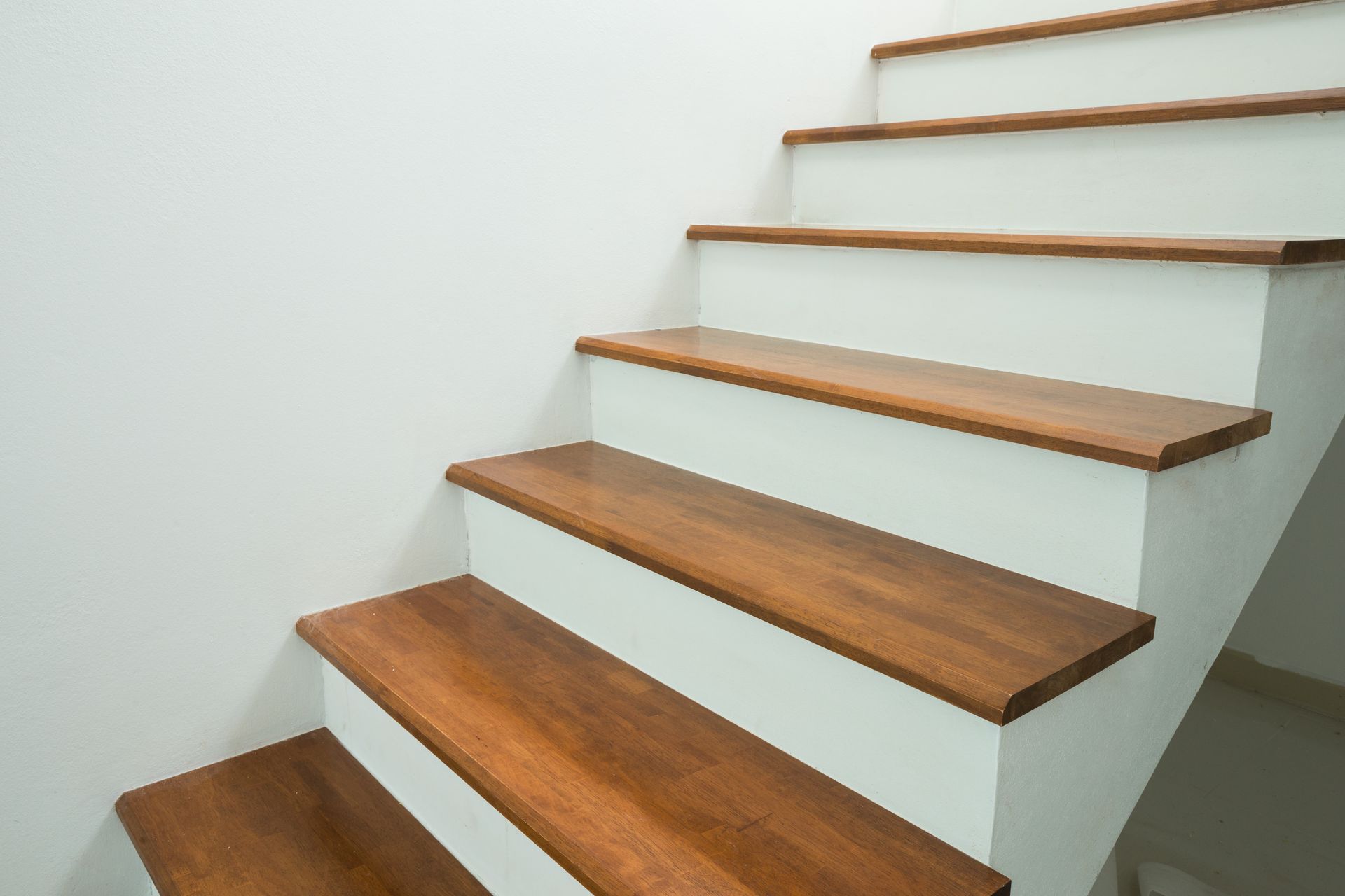 Wooden stairs with white risers ascending against a white wall.