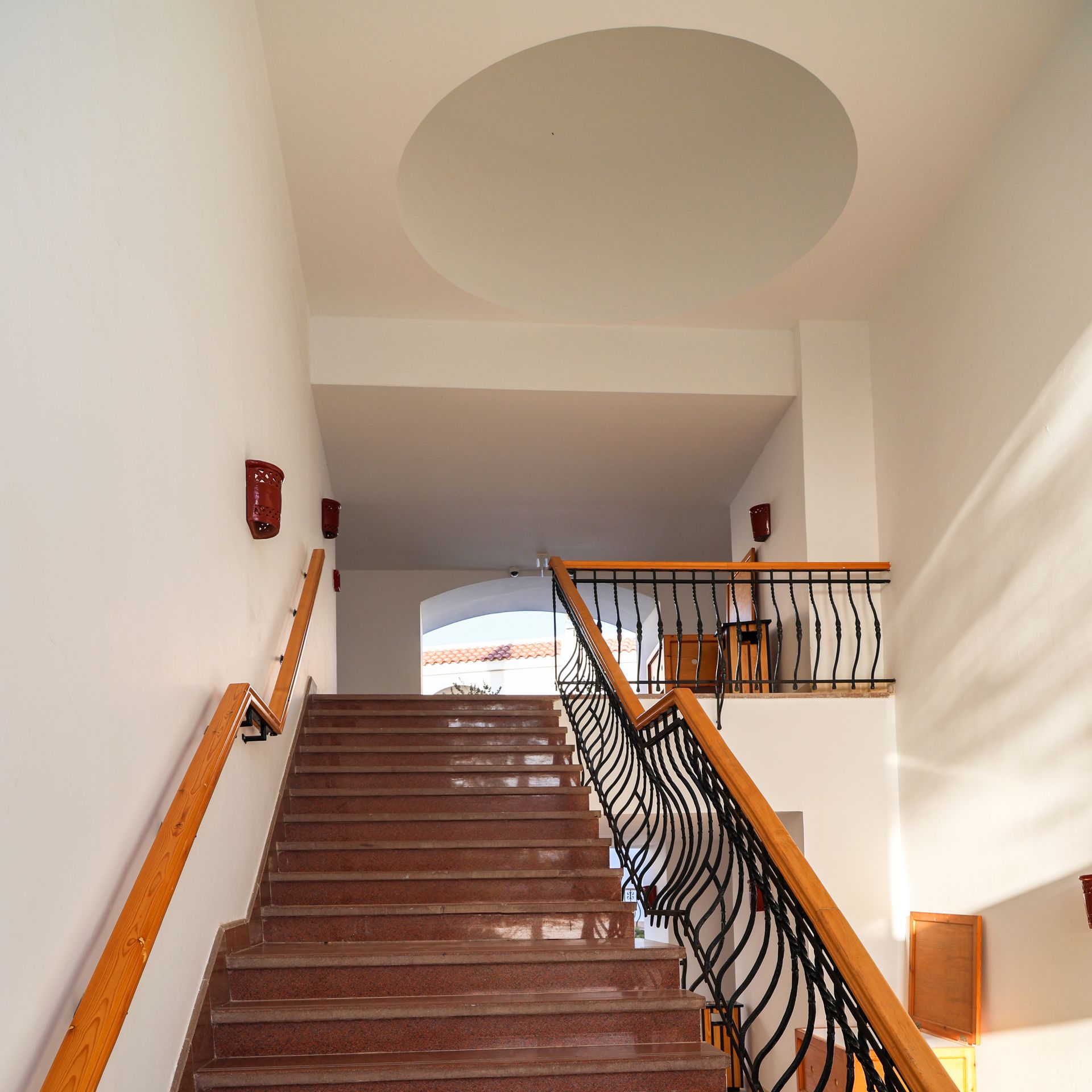Staircase with reddish-brown steps, wooden handrails, and black wrought iron detailing. White walls and ceiling.
