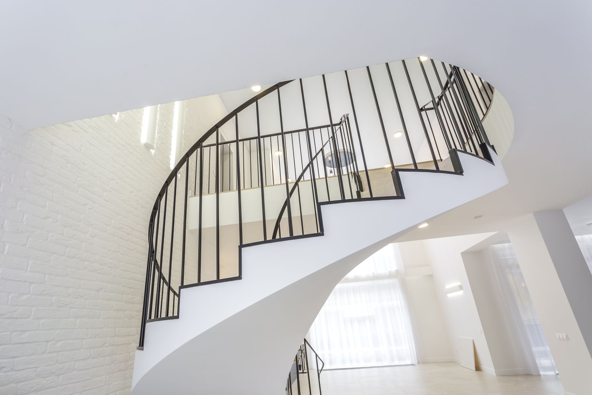 White, curved staircase with black railing ascending, set in a bright, modern interior.