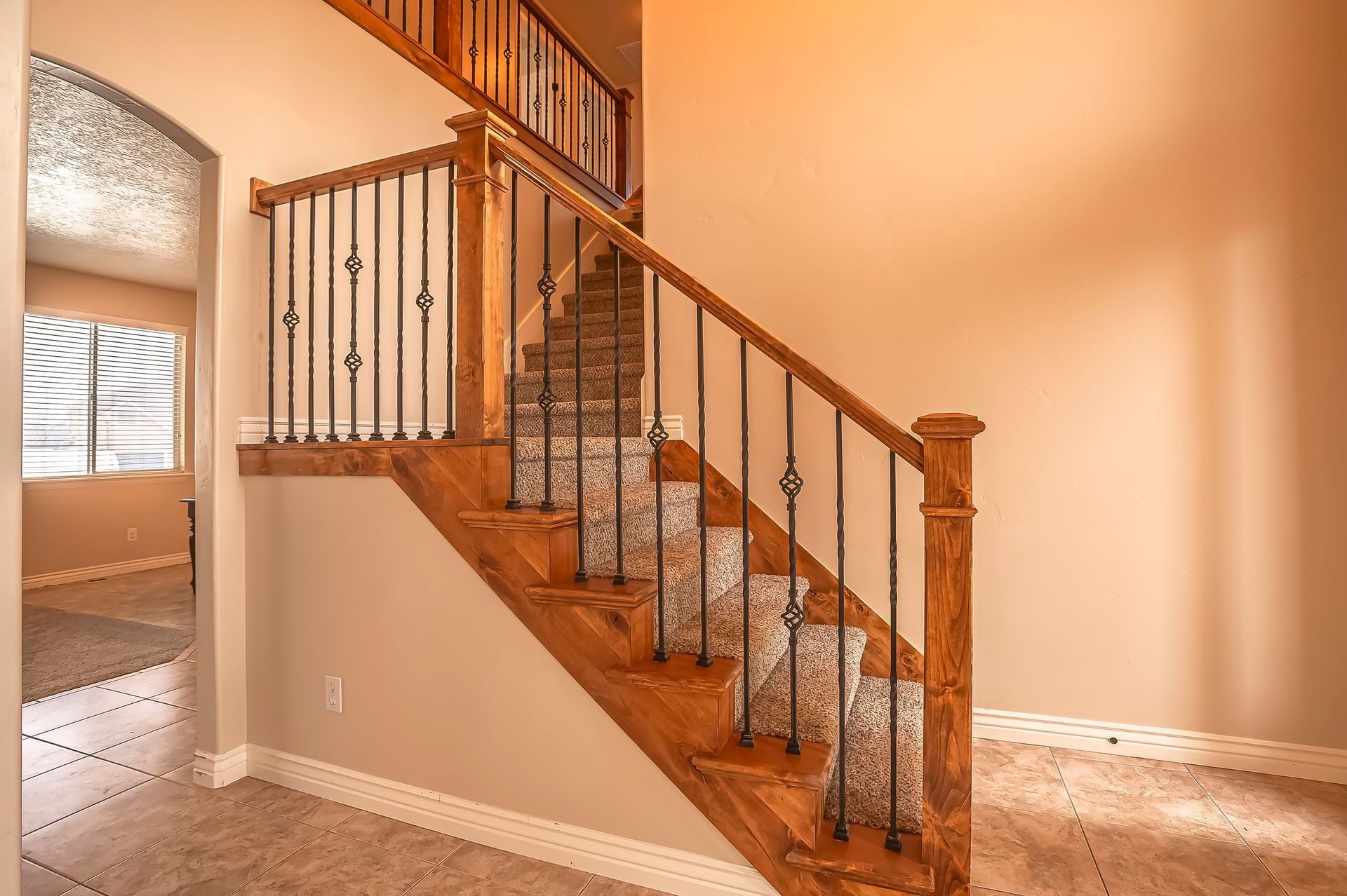 Wooden staircase with carpeted steps and wrought iron balusters in a neutral-toned foyer.