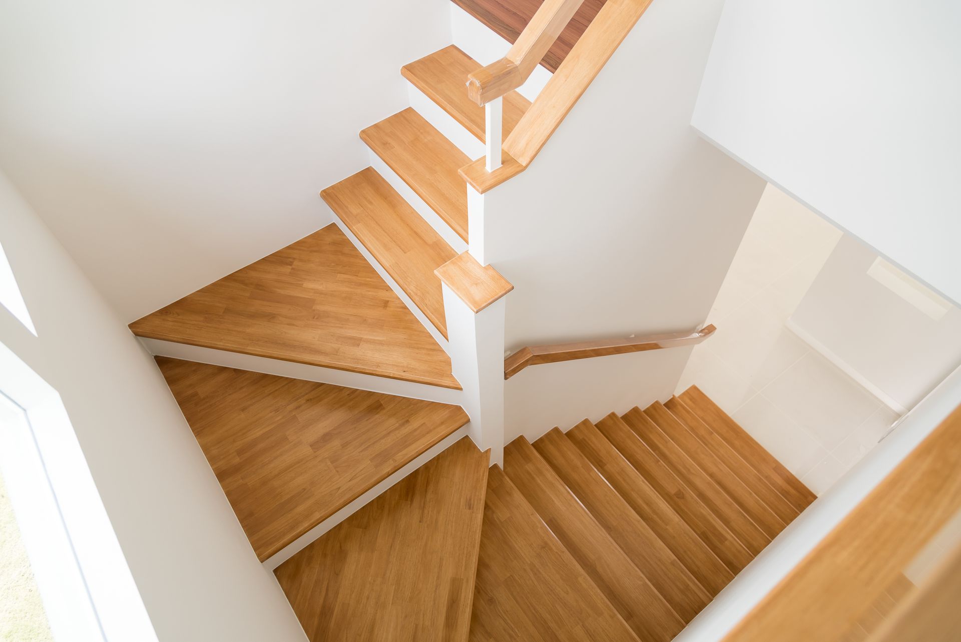 Wooden spiral staircase in a white-walled interior with a natural light source.