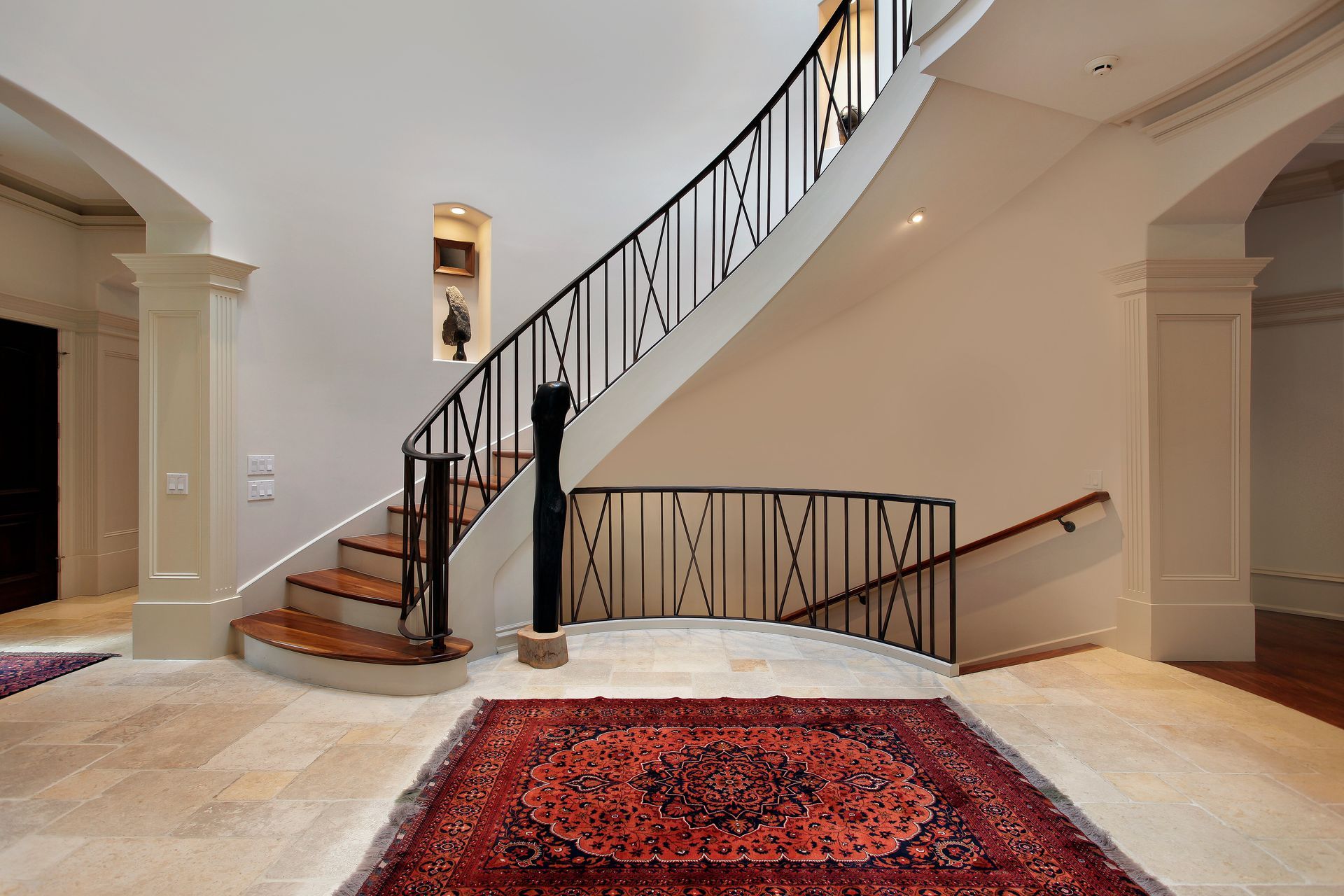 Elegant curved staircase with black railing, red rug, and stone floor.