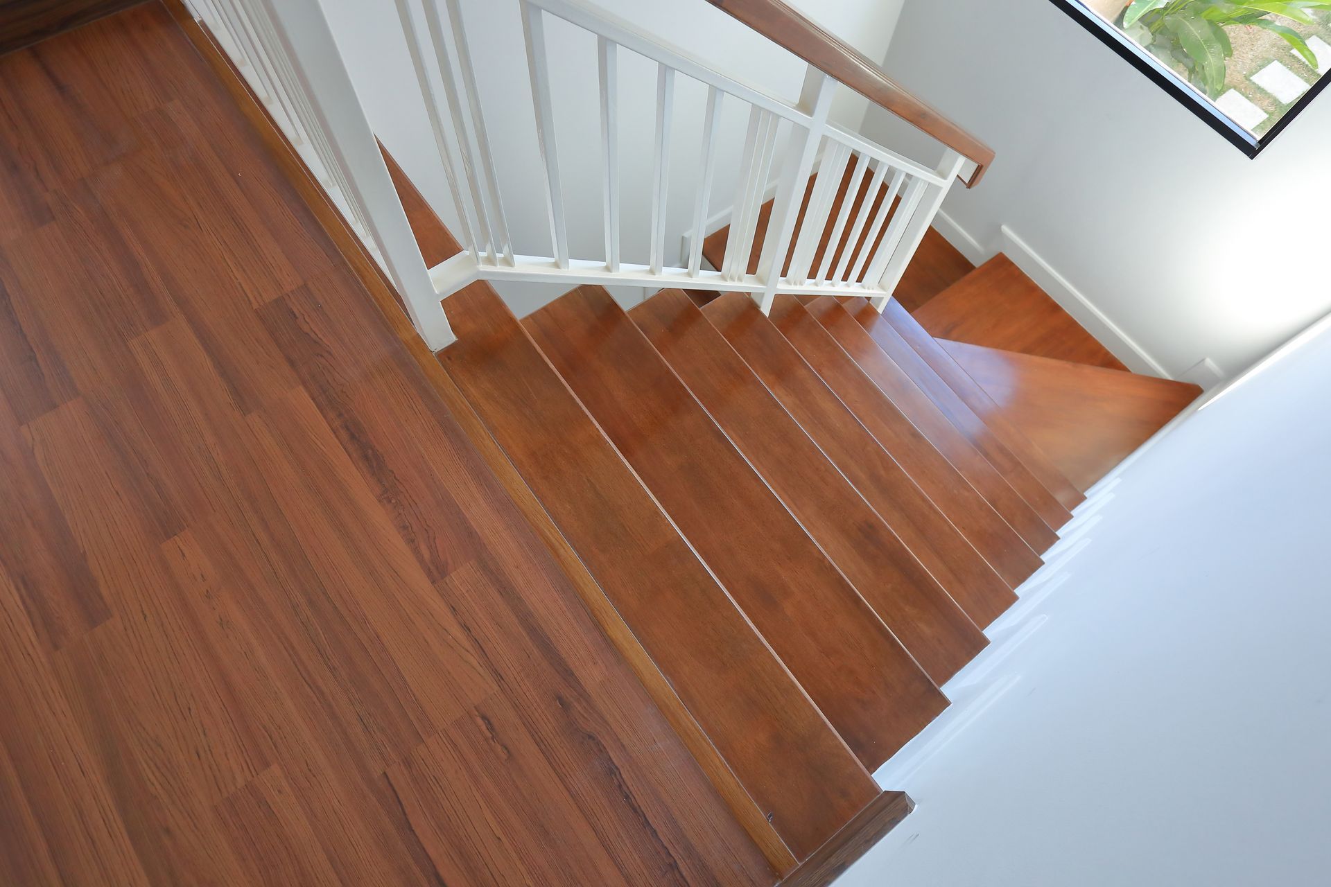 Wooden staircase with white banister, natural light from a window.
