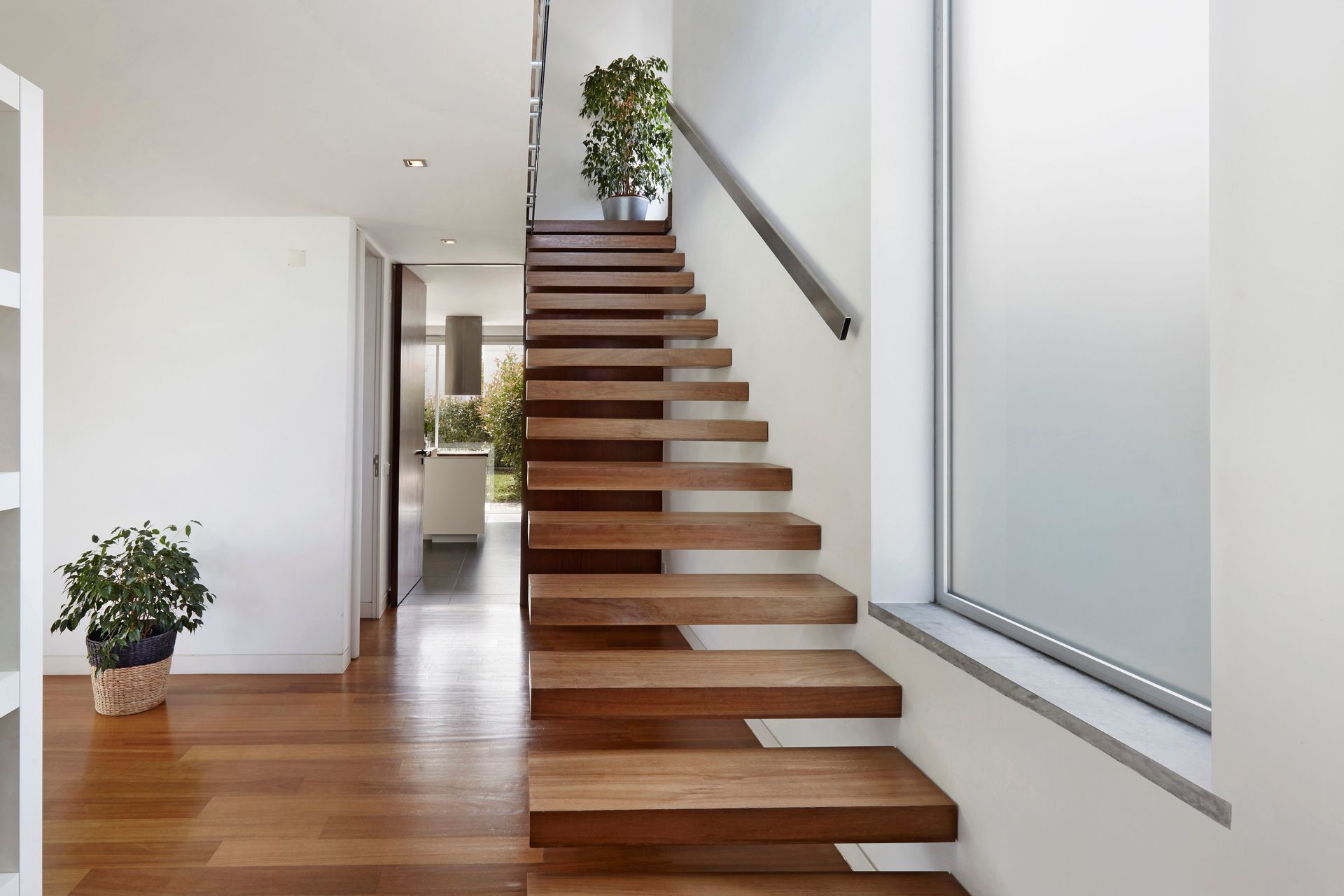 Wooden staircase in modern home with hardwood floors, leading upwards, near a window.